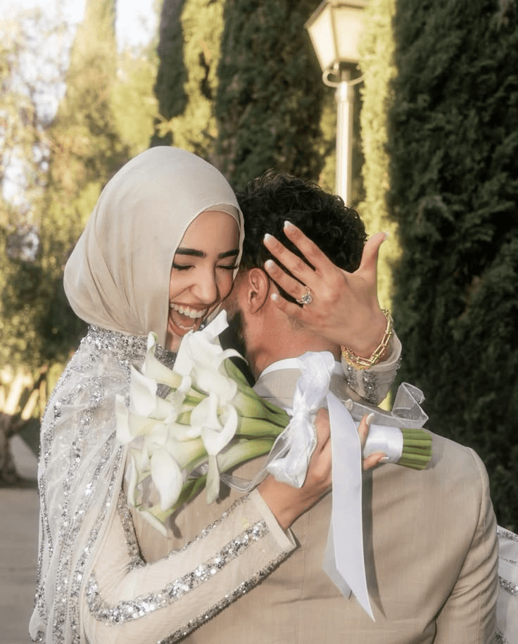 عروسان يتعانقان بفرح في الخارج، وهي تحمل زهورًا بيضاء